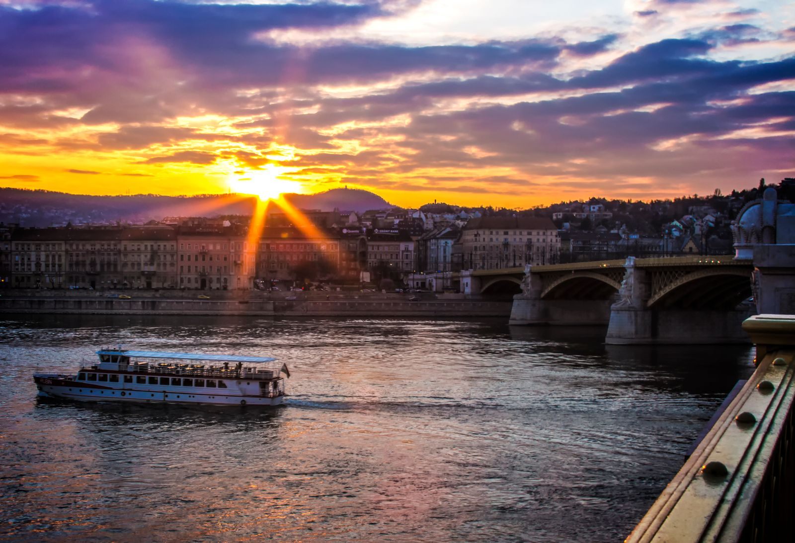 A riverboat on the Danube in Budapest at sunset beside the Margaret Bridge, the end of many affordable river cruises