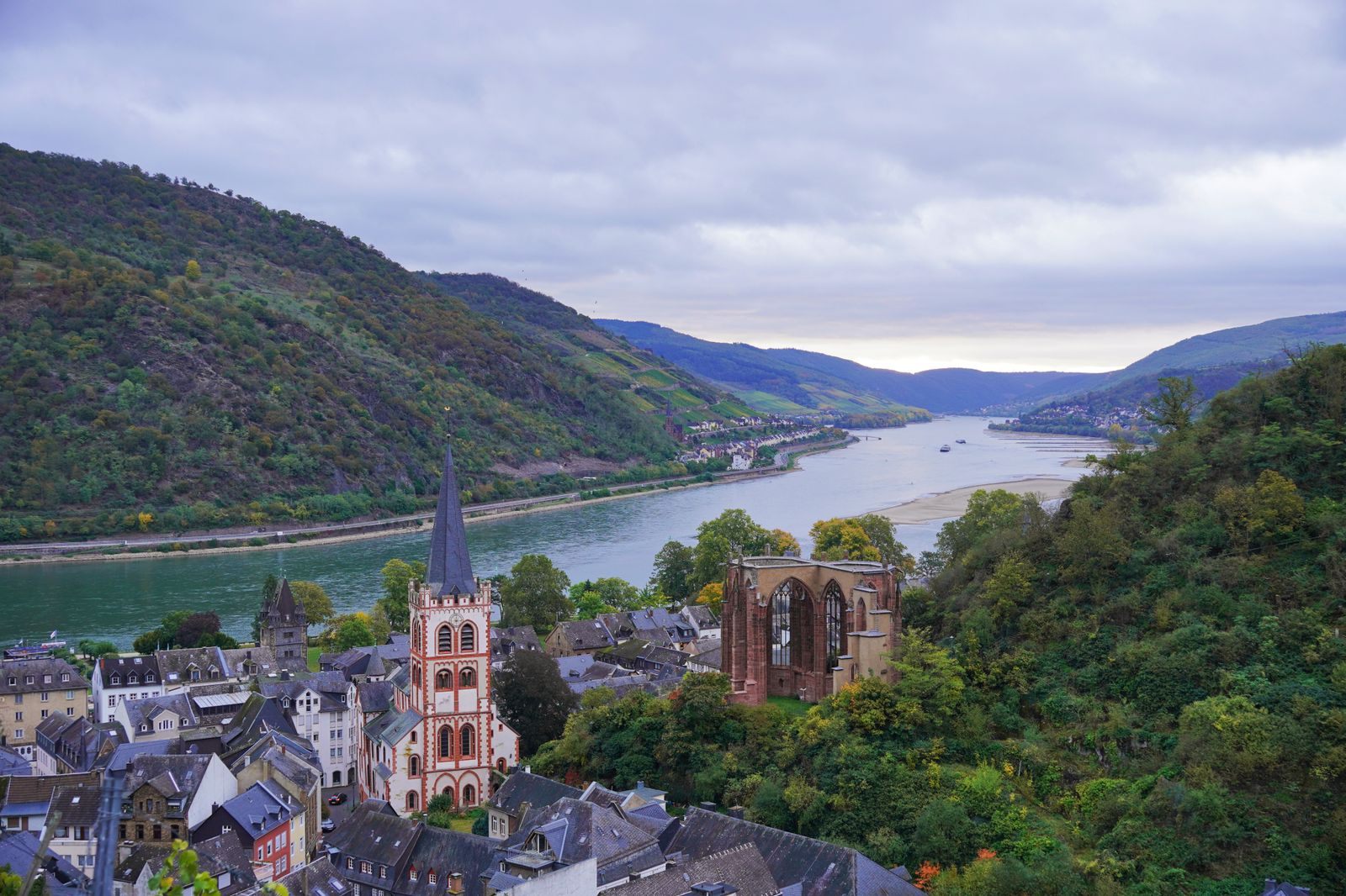 Bacharach’s church spire and chapel ruin beside the Rhine, with the river valley stretching away, a classic stop on cheap river cruises