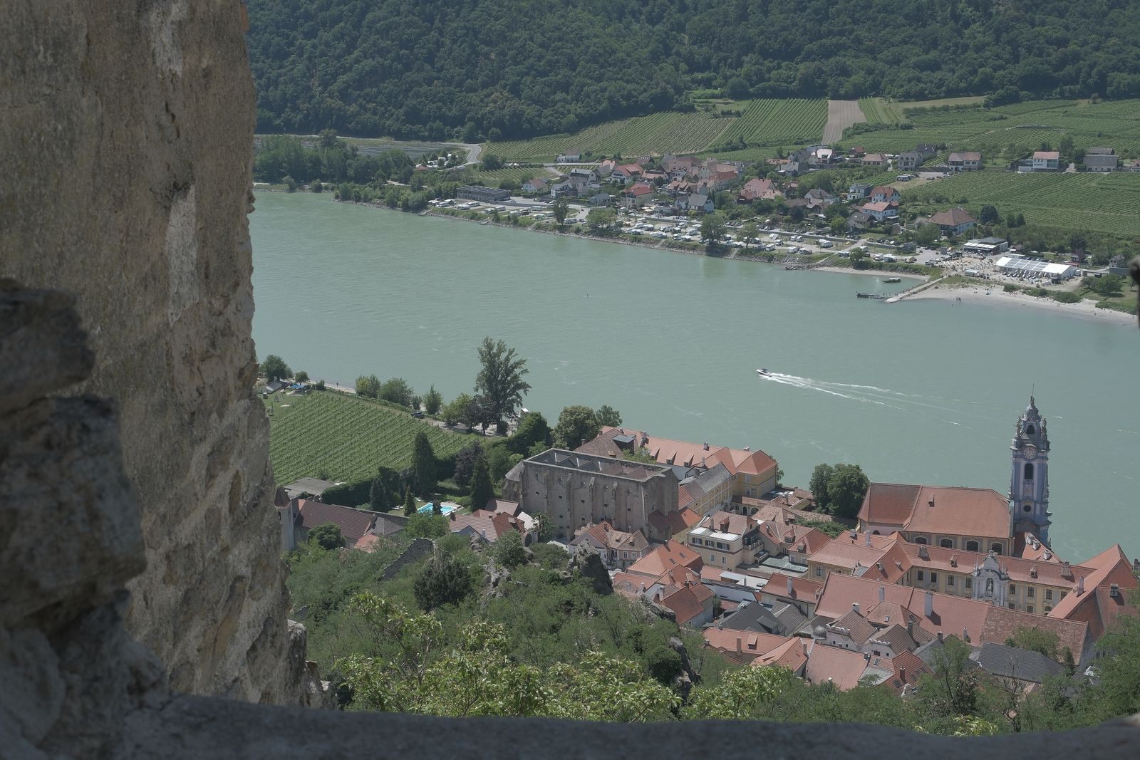 View through an old stone wall over Durnstein&rsquo;s blue church tower and the Danube in the Wachau, on many cheap river cruises in Europe