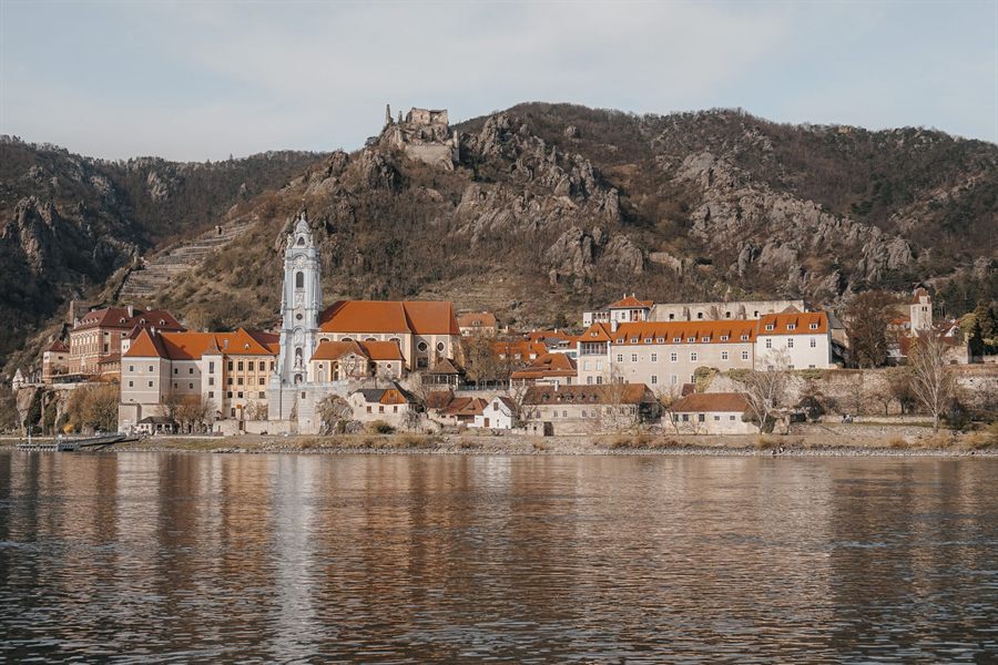 Durnstein Abbey and its blue tower reflected in the Danube below rocky hills